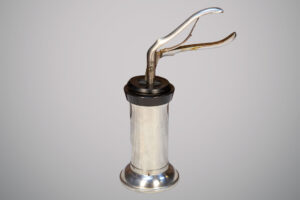 Instrumento médico antigo de metal prateado com base cilíndrica e alavanca superior em formato de pinça.