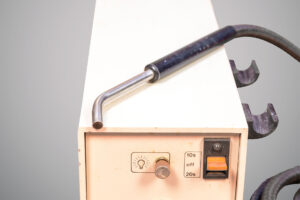 Equipamento odontológico retangular da marca Dentsply, de cor bege, com cabo grosso preto ligado a uma peça metálica cilíndrica. Na frente há um botão prateado com símbolo de lâmpada, um seletor com as opções “dez segundos”, “off” e “vinte segundos”, além de uma chave laranja de liga e desliga.