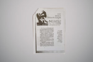 Página de revista com o título “História da Odontologia”, trazendo um texto explicativo sobre a origem da profissão e uma imagem em preto e branco de um homem aparentemente realizando um procedimento dentário em outro, que está sentado e expressa dor.