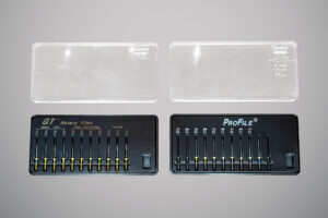 Conjunto de limas endodônticas em estojos pretos, um à esquerda com a marca GT Rotary Files e outro à direita com a marca ProFile, ambos com fileiras de instrumentos metálicos finos organizados por tamanho e espessura, acompanhados de tampas transparentes.