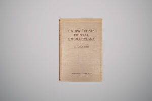 Capa dura bege de um livro antigo com o título centralizado em letras maiúsculas “La prótesis dental en porcelana”, seguido pelo nome do autor “A. L. Le Gro” e, abaixo, o nome da editora “Editorial Labor, S. A.”.