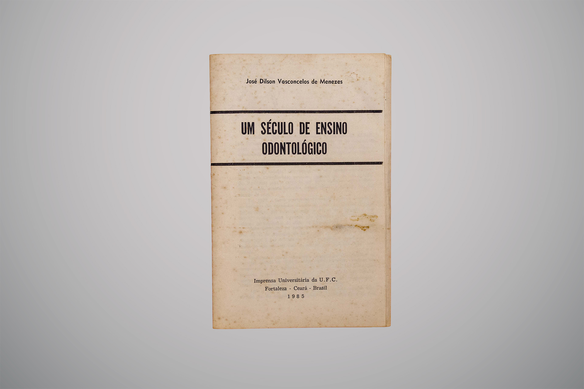 Capa envelhecida do livro “Um Século de Ensino Odontológico”, de José Dilson Vasconcelos de Menezes, publicado em mil novecentos e oitenta e cinco pela Imprensa Universitária da Universidade Federal do Ceará.