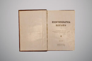Página interna de livro antigo com fundo bege; à direita, há um retrato em tom sépia de um homem de barba cheia, identificado abaixo como "Wilhelm Conrad Röntgen".